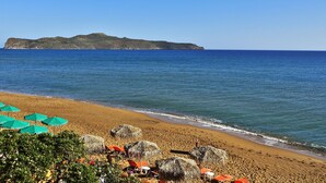 A beach with umbrellas and chairs, a clear view of the sea, and a distant island. - Hermes Beach Front (Chania)