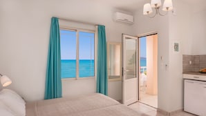 A bedroom with a bed, a window with curtains, a door leading to a balcony, and a kitchenette. - Hermes Beach Front (Chania)