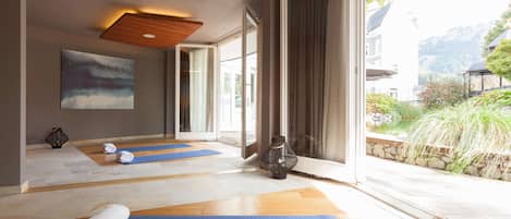 Un salón de yoga con suelo de madera, esterillas azules y un ventanal con vistas a zonas verdes y edificios.