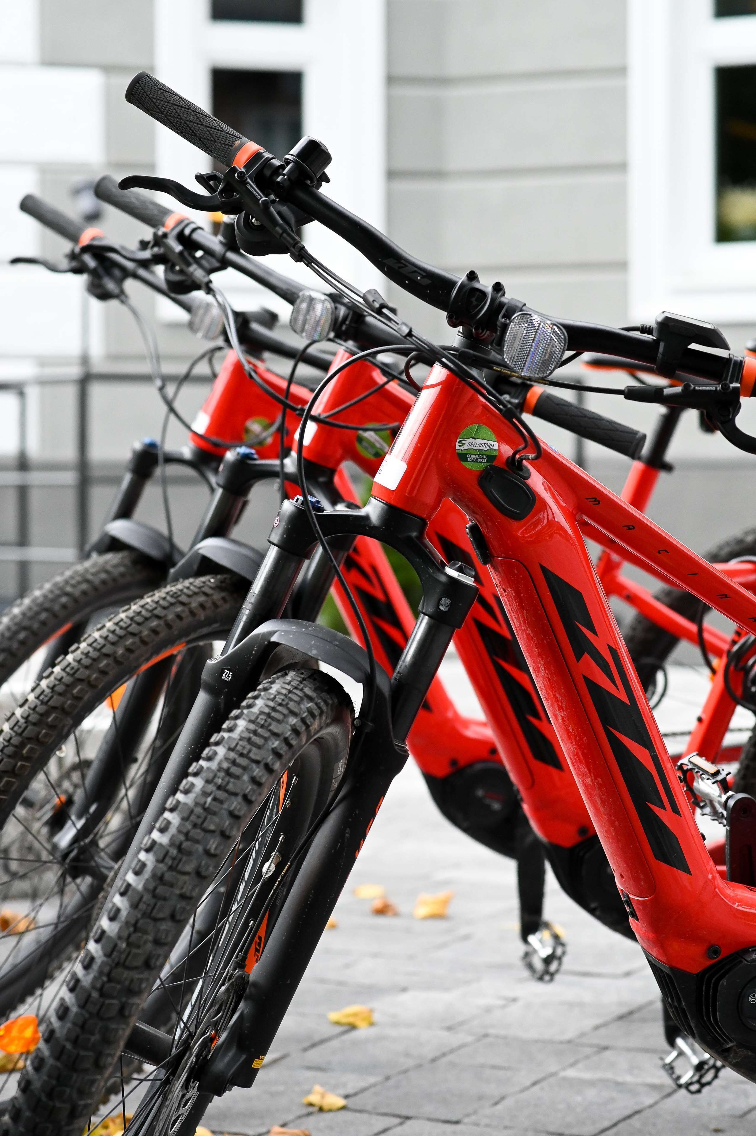 A row of red mountain bikes parked in an outdoor area with a building in the background.