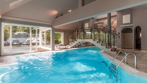 Una piscina interior con barandillas de vidrio, una escalera y vistas de mobiliario exterior.