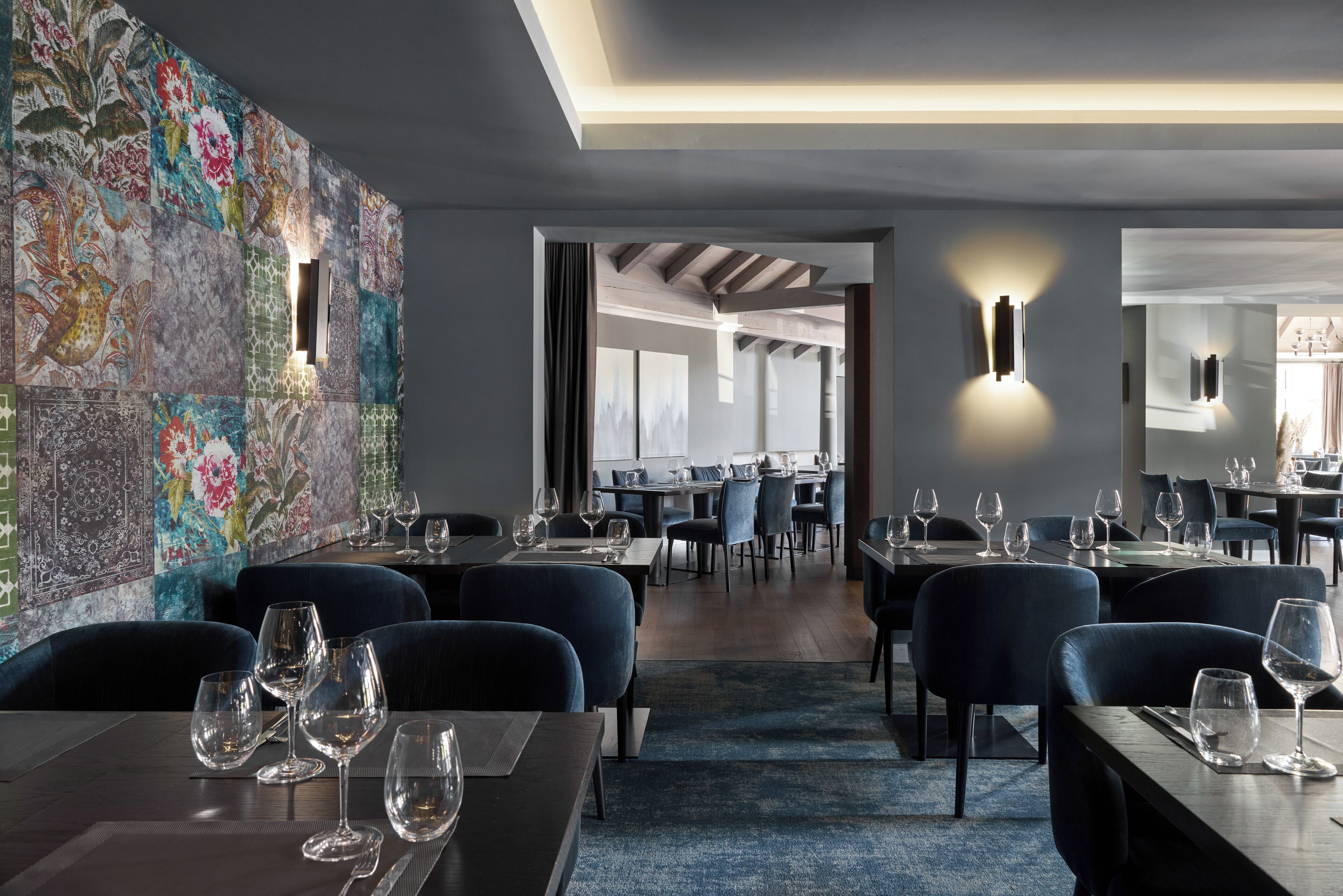 A modern restaurant interior with a patterned wall, dark seating, and tables set with wine glasses.