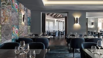 A modern restaurant interior with a patterned wall, dark seating, and tables set with wine glasses.