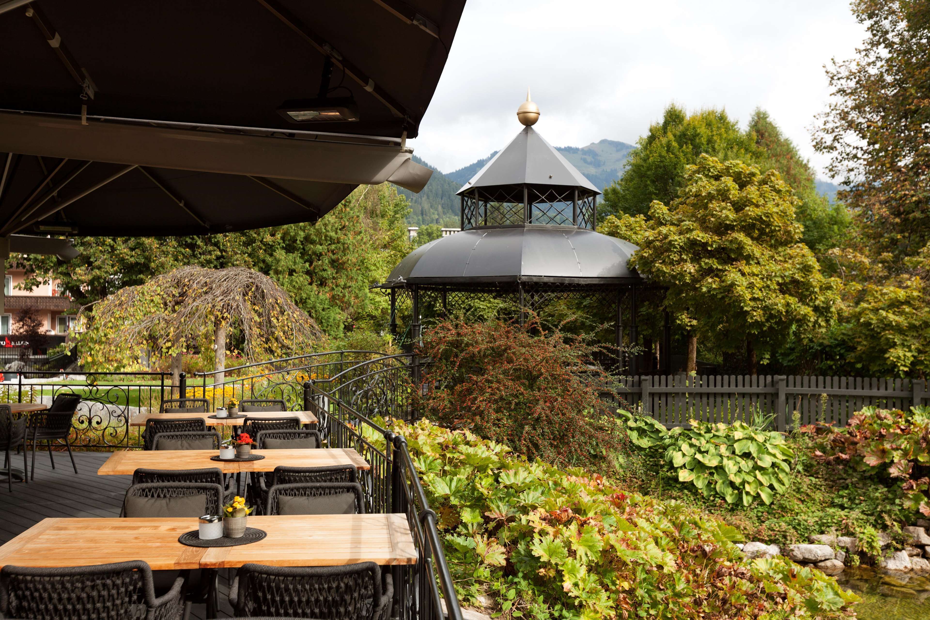 An outdoor dining area with tables and chairs, surrounded by lush greenery and a mountain backdrop.