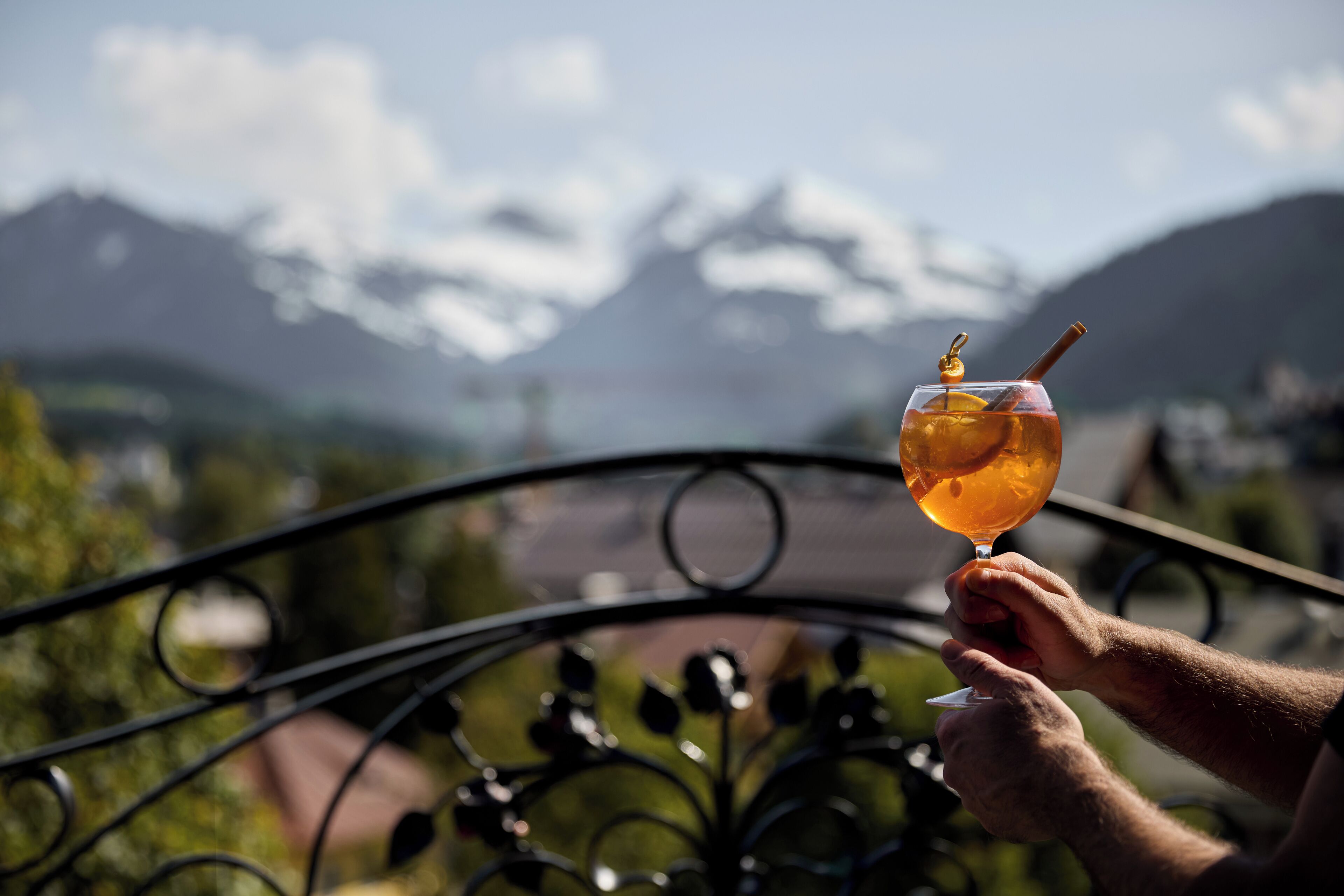 A person holding a glass with a drink, overlooking a mountainous landscape.