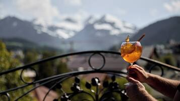 A person holding a glass with a drink, overlooking a mountainous landscape.