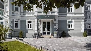 En elegant hotellentrén med en skylt som visar texten ”Erika Boutique Hotel”, en asfalterad uppfart och två statyer föreställande rådjur.
