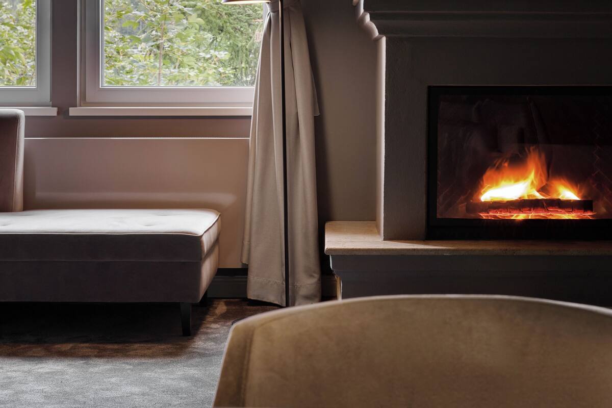 Una sala de estar moderna con chimenea, un sofá y vistas a zonas verdes a través de amplios ventanales.