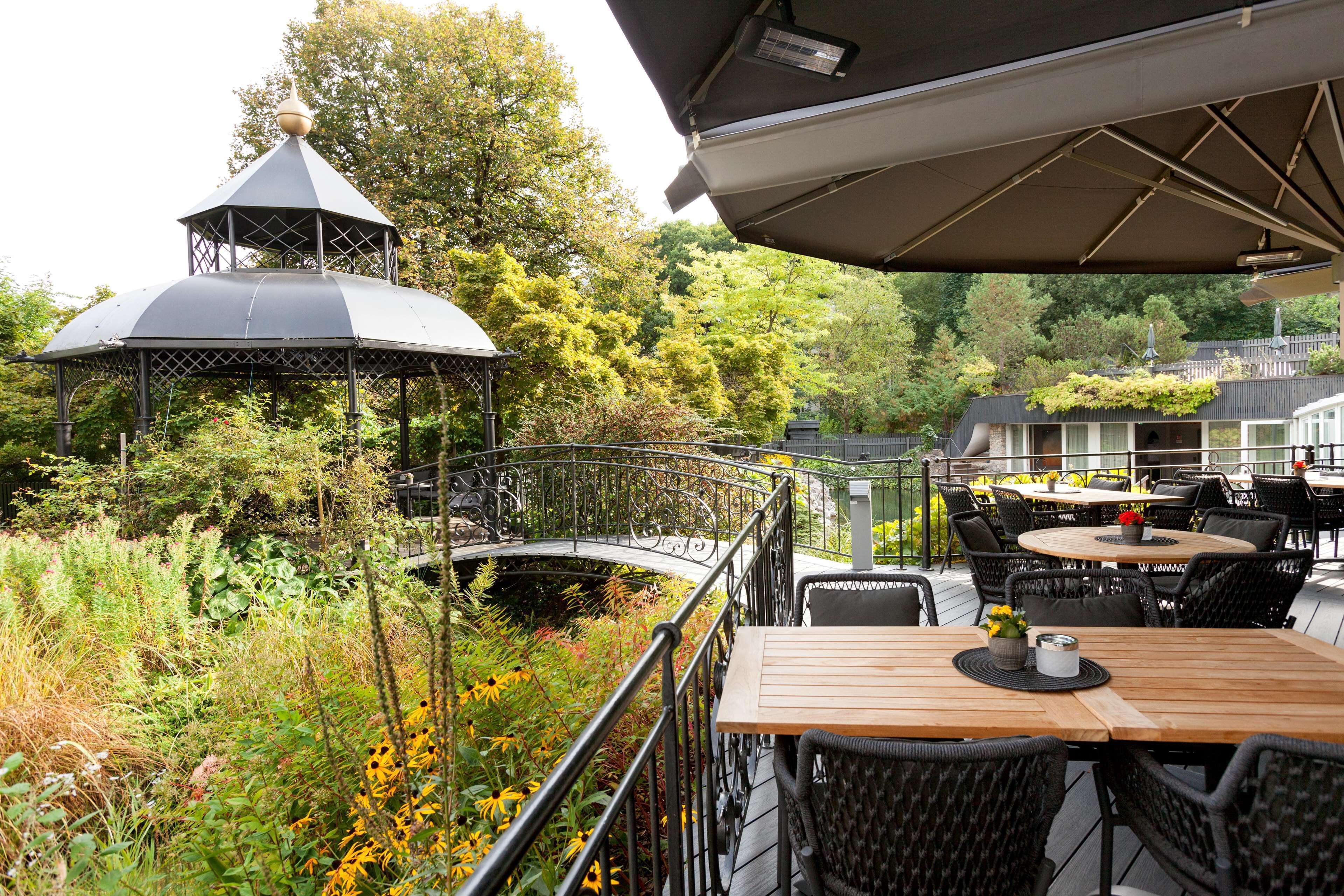 Un belvédère surmonté d’un dôme, entouré d’une végétation luxuriante et doté d’une terrasse en bois avec des sièges d’extérieur.