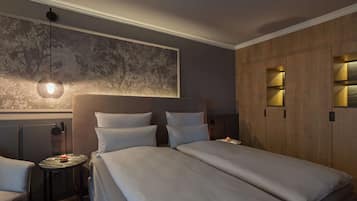 Habitación de hotel con dos camas, una mesita, una silla, una obra de arte en la pared y estanterías empotradas con iluminación.