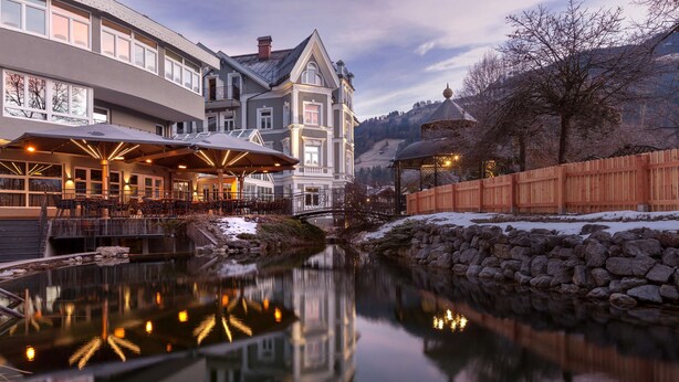 Un hotel con su reflejo en un cuerpo de agua tranquila, una pared de piedra y una valla de madera.