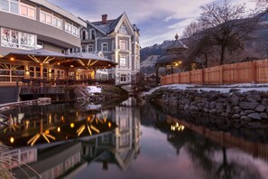 Un hotel con su reflejo en un cuerpo de agua tranquila, una pared de piedra y una valla de madera.