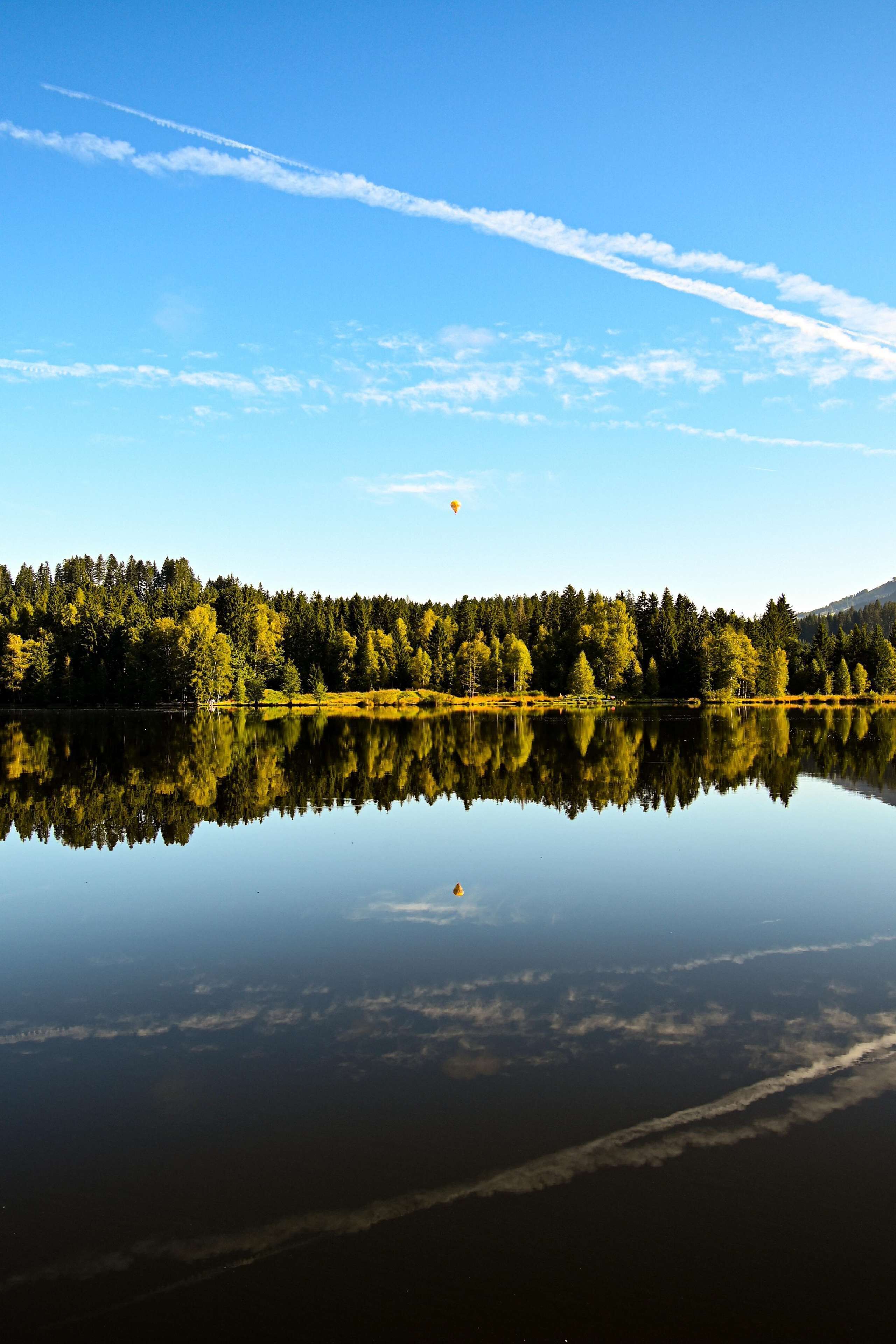 A calm lake with a clear reflection of trees and a sky with clouds.