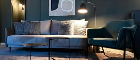 A modern living room with a sofa, a round coffee table, and a chair. There is a painting on the wall and a floor lamp.