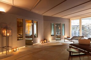 Zona de spa con una mesa de masaje, velas y una sauna visible a través de un vidrio.