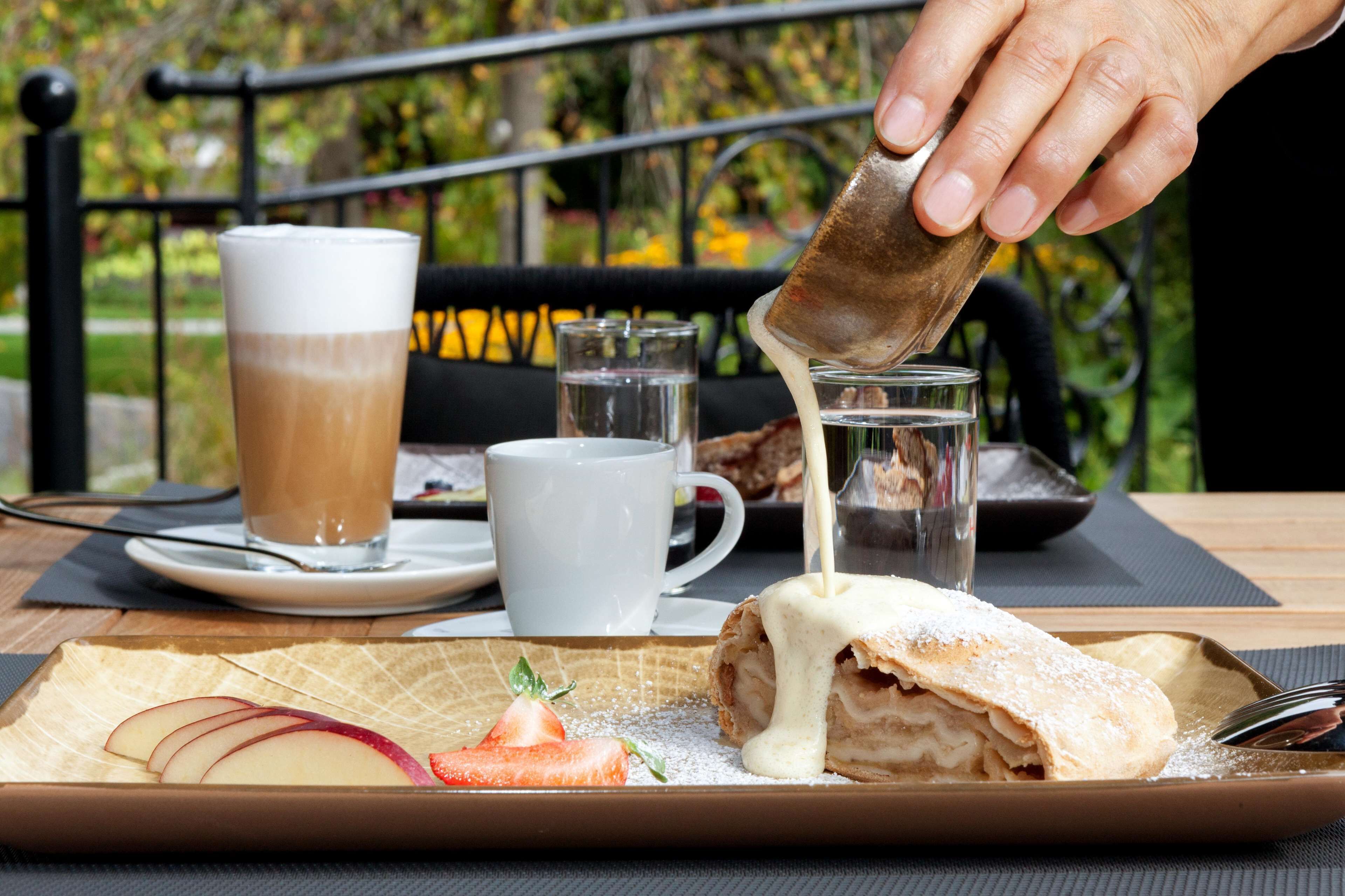 Un plato con un pastel, una taza de café y un vaso de agua sobre una mesa al aire libre.