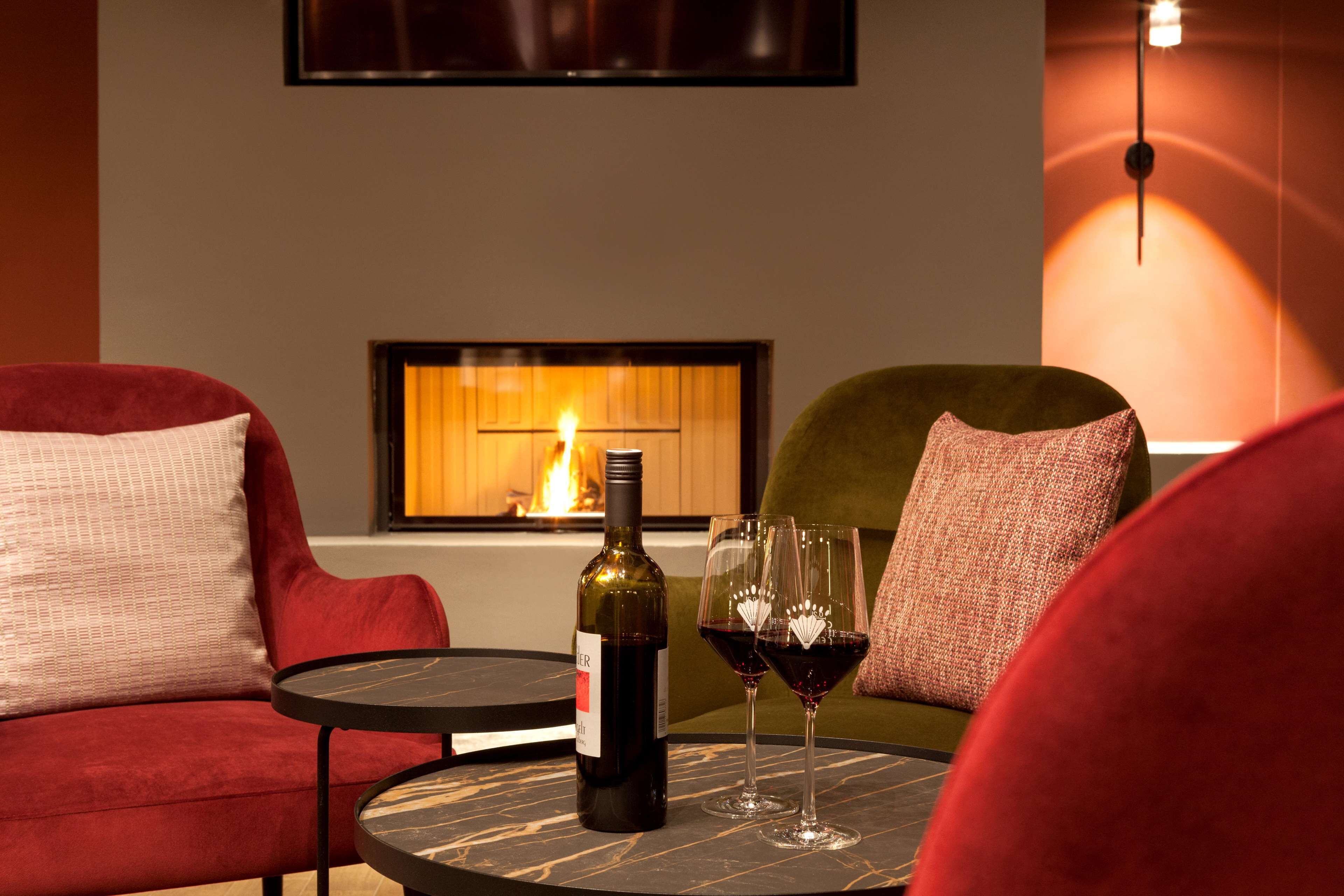 A cozy seating area with a fireplace, a bottle of wine, and two wine glasses on a round table.