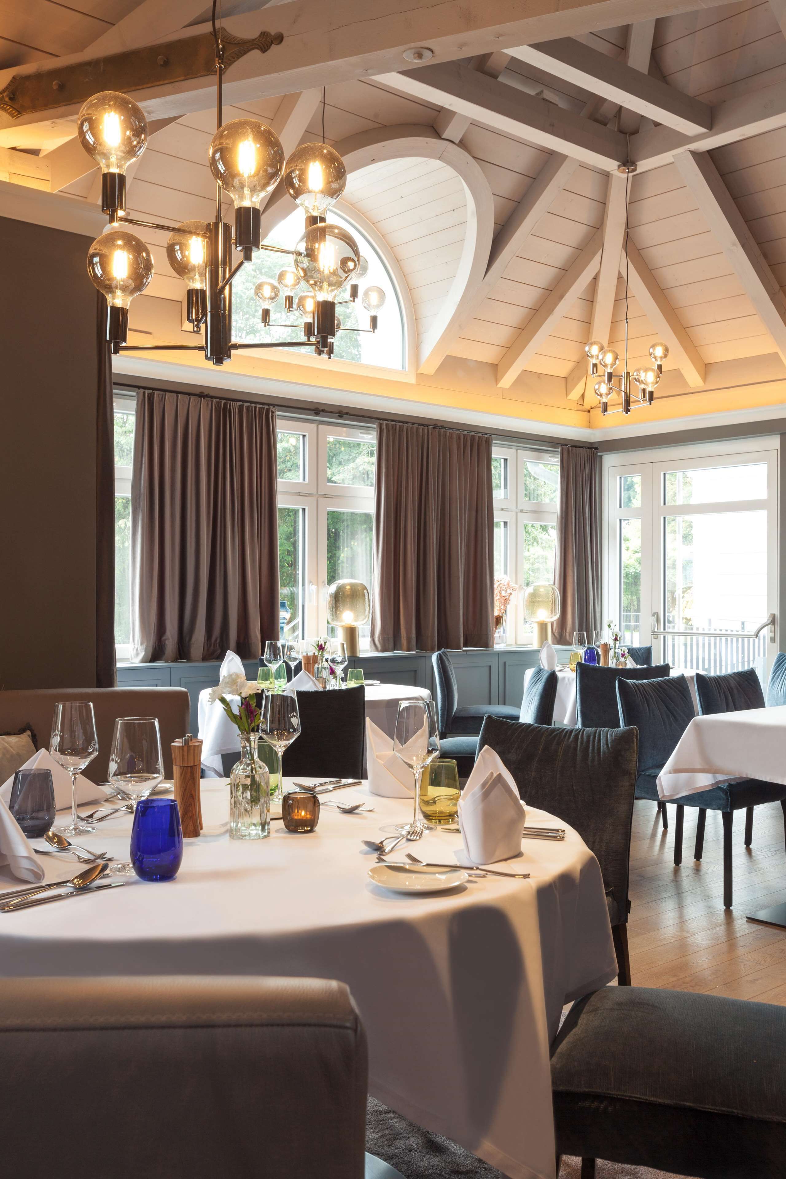 A dining area with round tables, chairs, and hanging light fixtures.