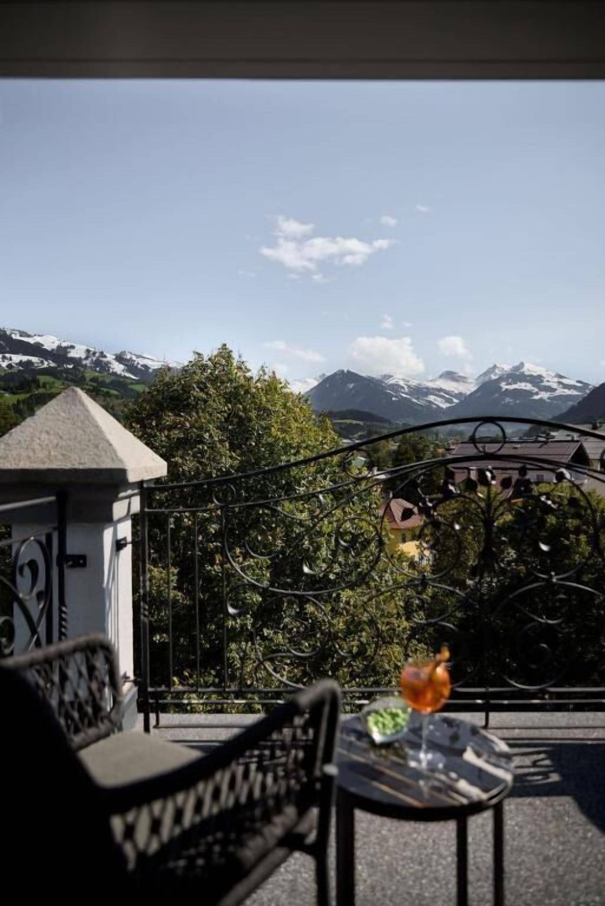 A balcony with a table and chairs, a glass of drink, and a view of snow-capped mountains.