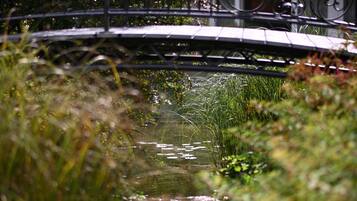 Een metalen brug over een smalle watergang, omgeven door weelderige begroeiing.