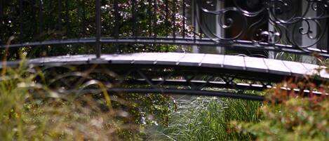 Un puente metálico cruza un estrecho canal de agua rodeado de vegetación densa.