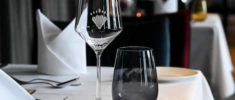 A dining table with a wine glass and a bowl, set with cutlery and a napkin.