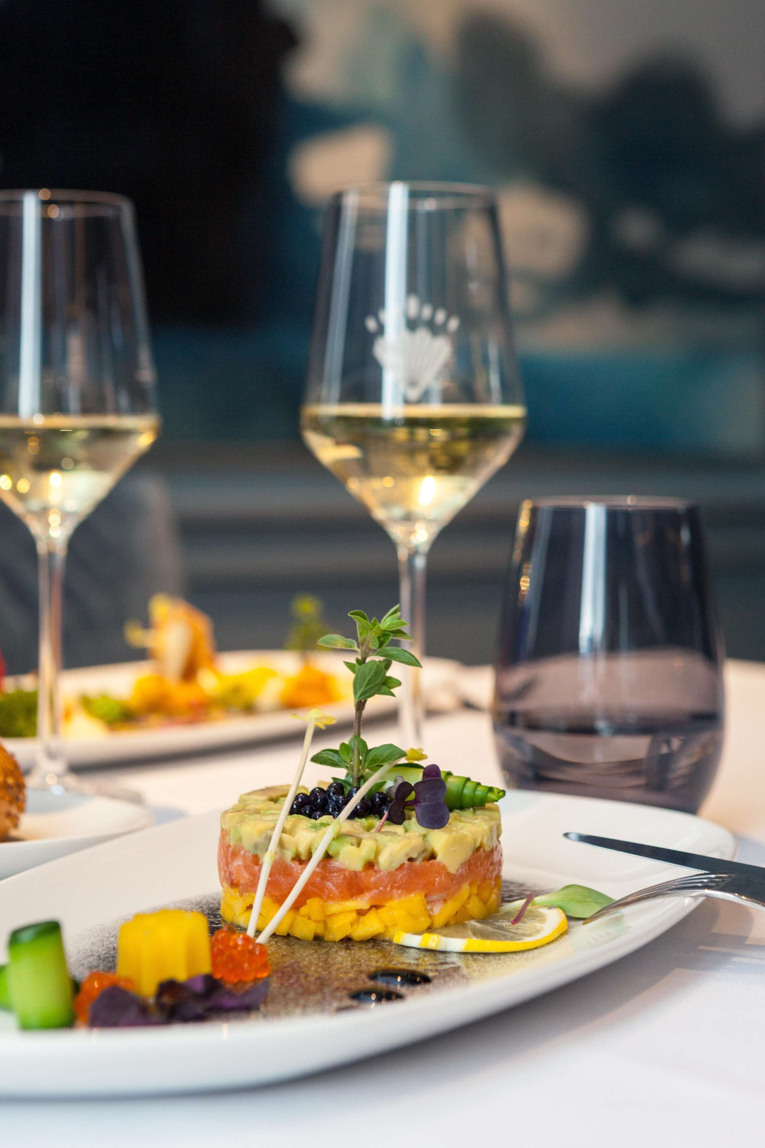 Una mesa de comedor con un plato servido y dos copas de vino blanco.