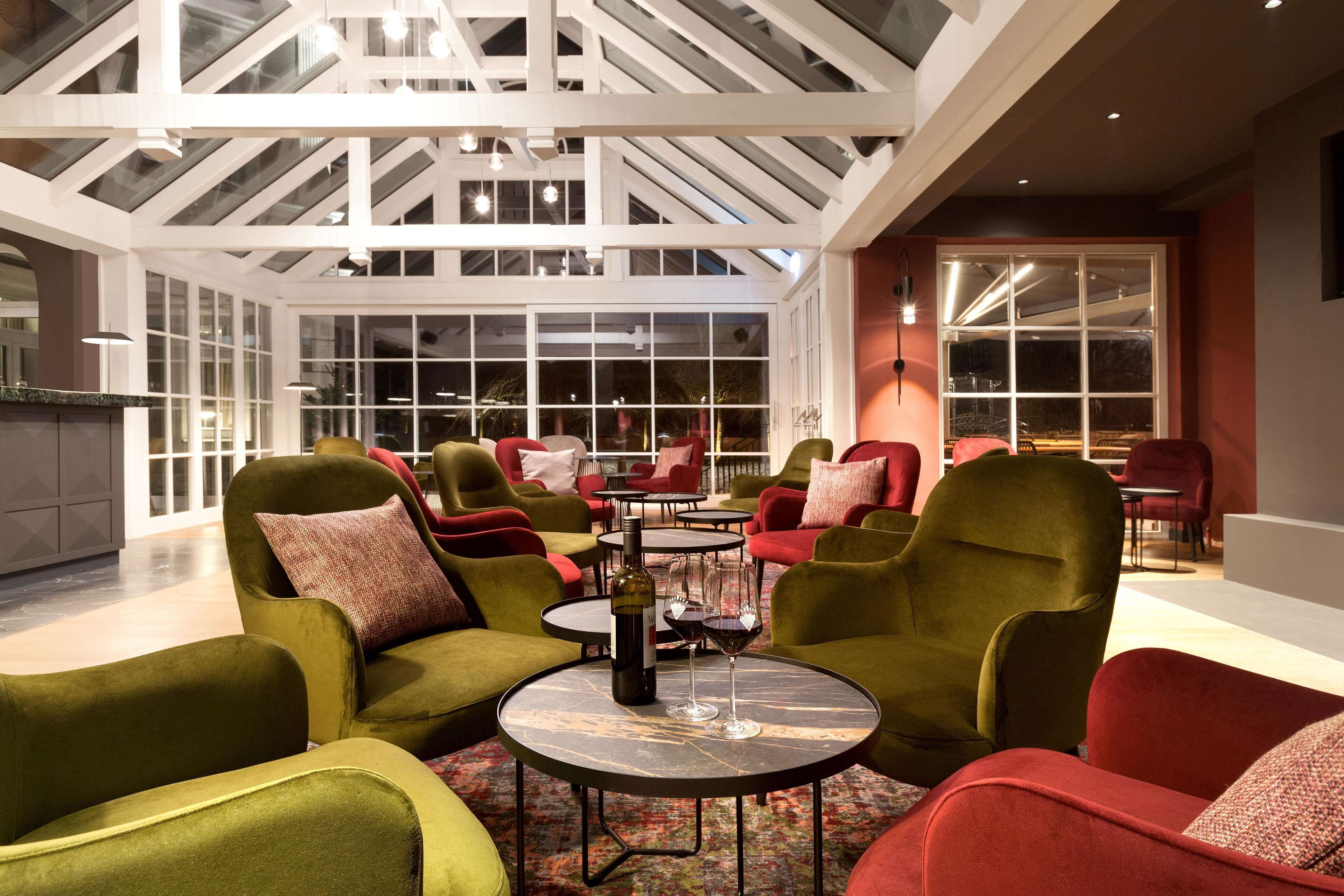 A spacious indoor area with multiple seating arrangements, including sofas and chairs, and a central table with a bottle and glass.