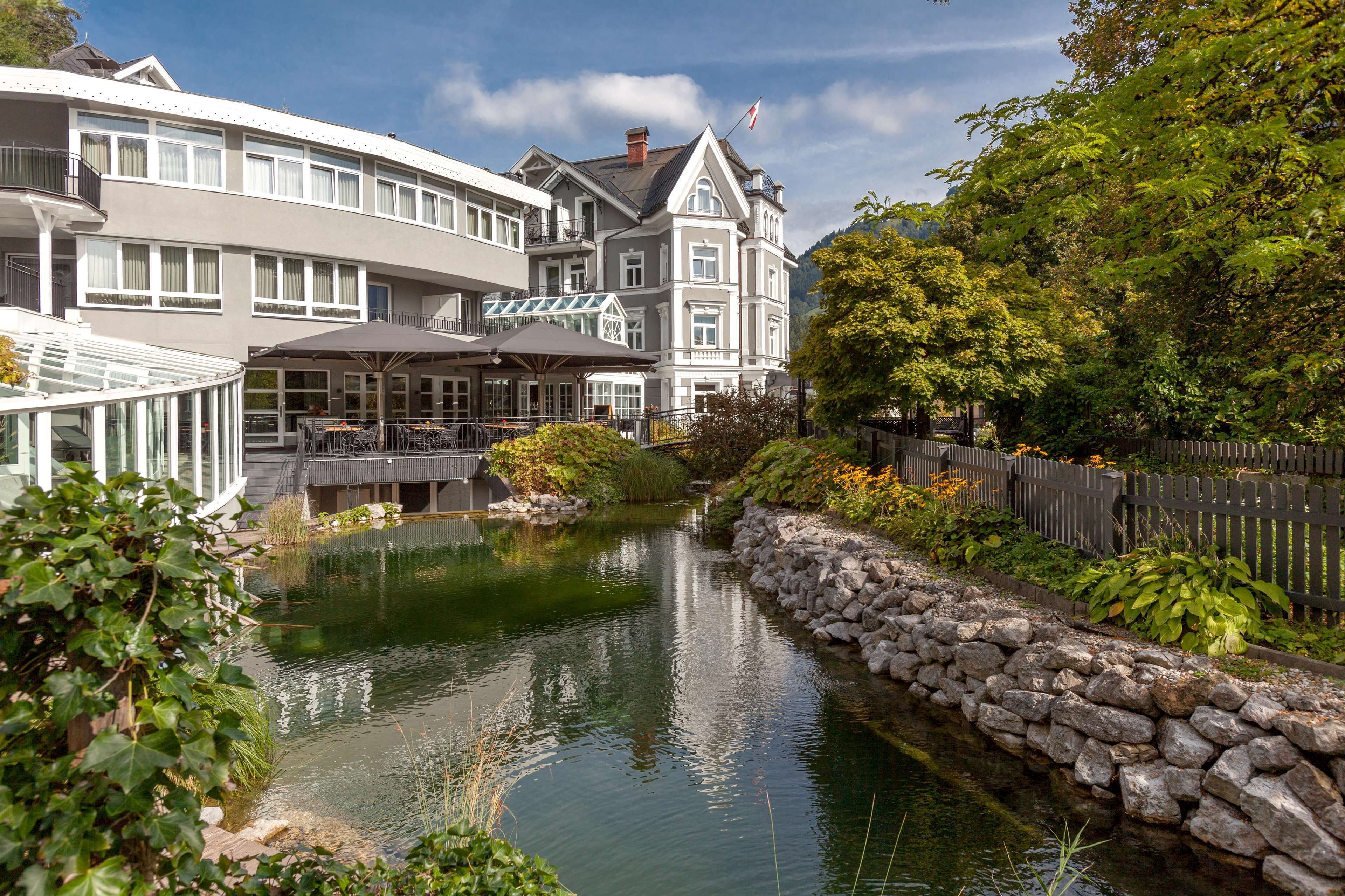 A riverside hotel with a stone wall, a glass conservatory, and a wooden deck.