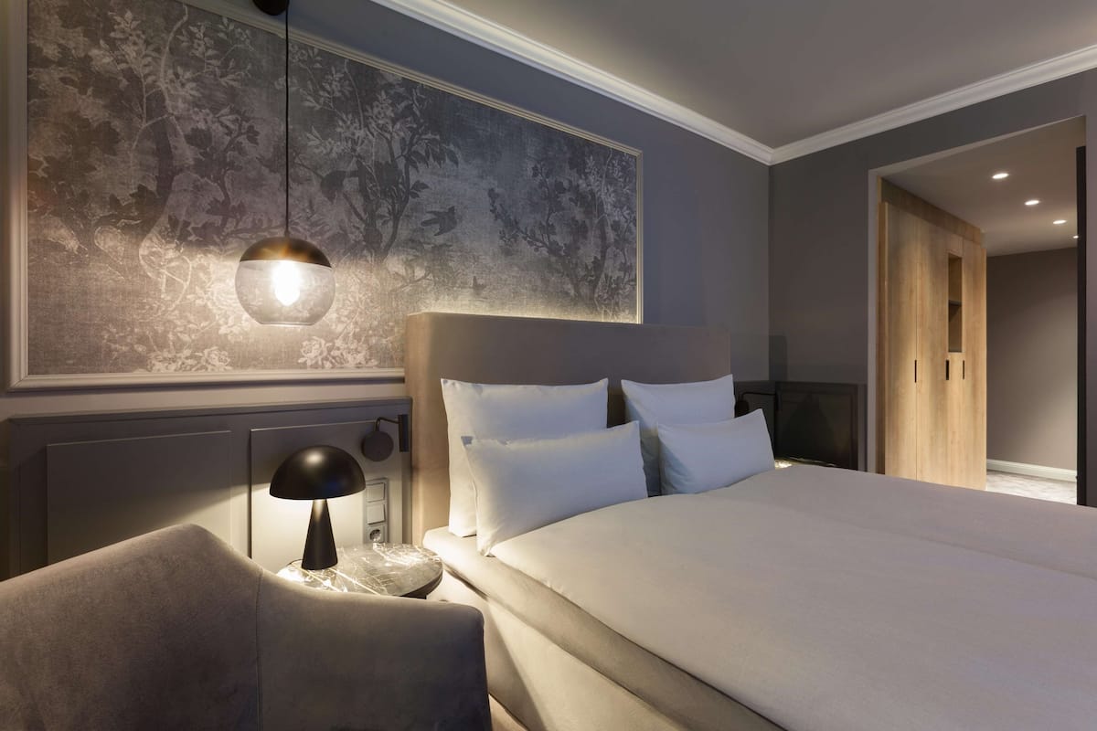 Una habitación de hotel moderna con una cama grande, una mesita de noche con lámpara y una obra de arte colgada en la pared.