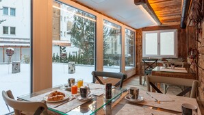 A dining area with a glass table, chairs, and a view of a snowy outdoor scene through large windows.