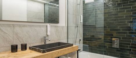Un baño moderno con tocador de madera, cabina de ducha de vidrio y pared con azulejos de mármol.