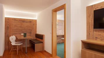 A compact room with a wooden wall, a small table with a bench, a white chair, and a television mounted on the wall.