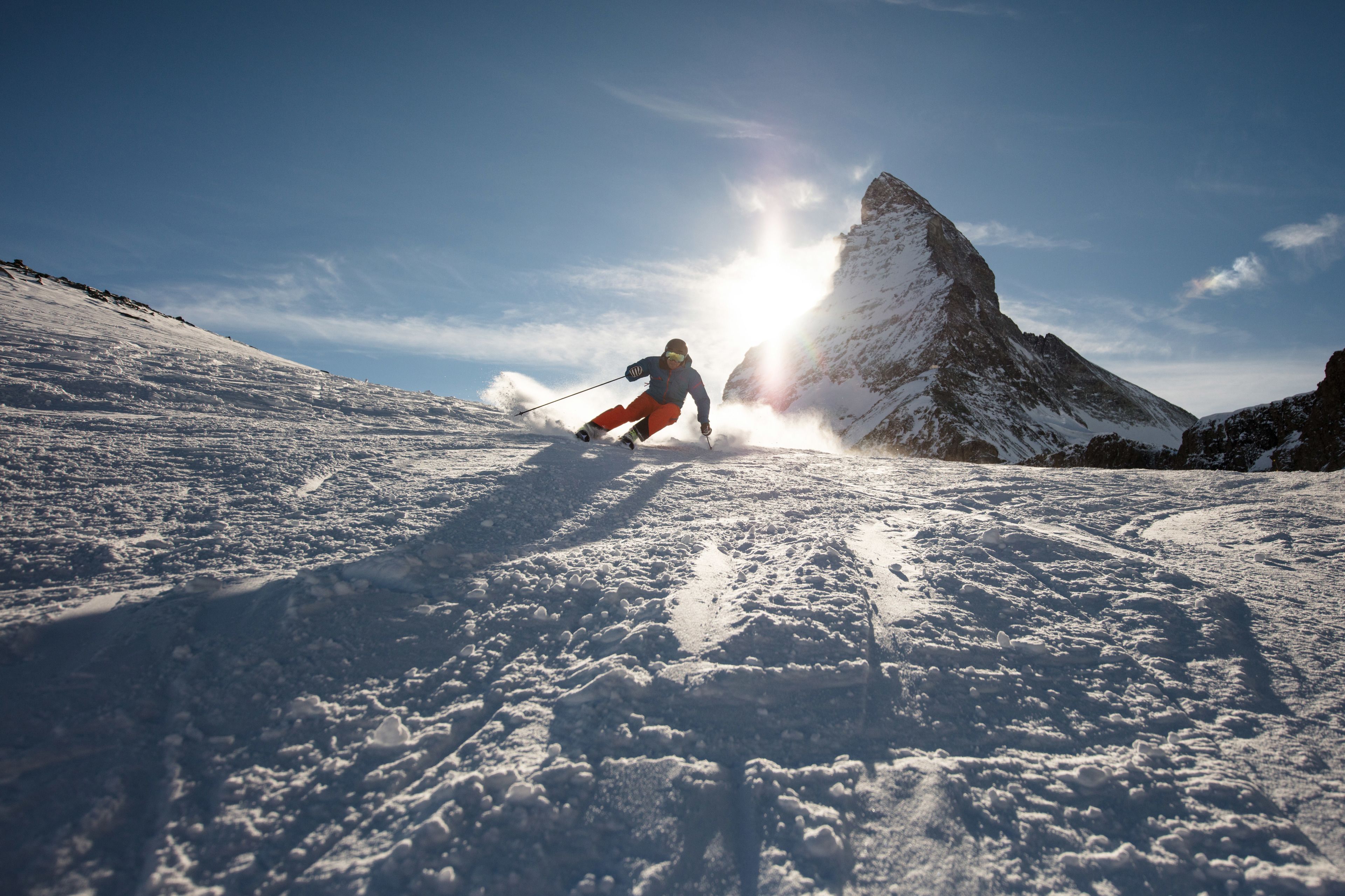 Un skieur sur une pente enneigée, avec une montagne en arrière-plan.