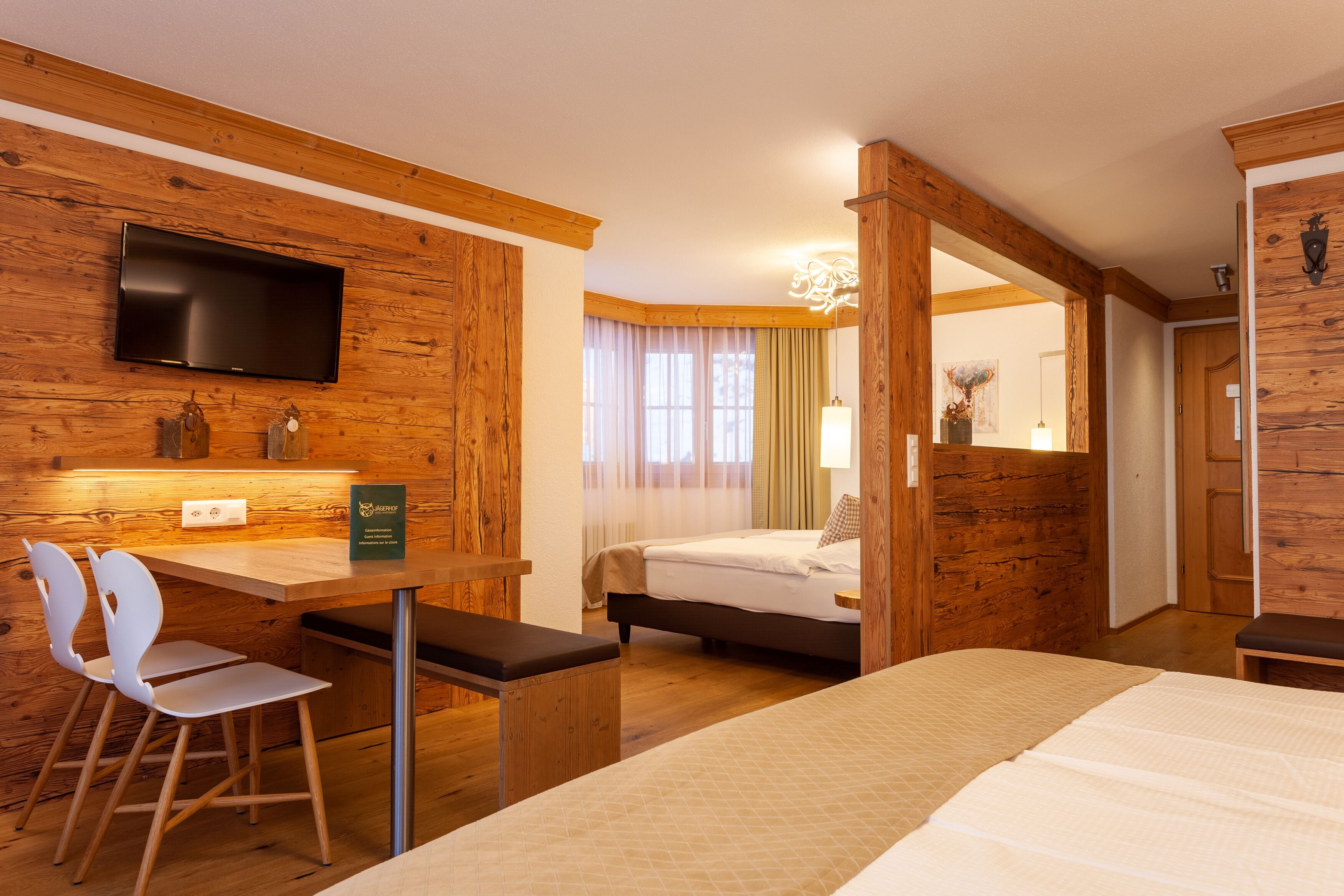 A hotel room with a wooden interior, a bed, a desk with a chair, a television mounted on the wall, and a window with curtains.