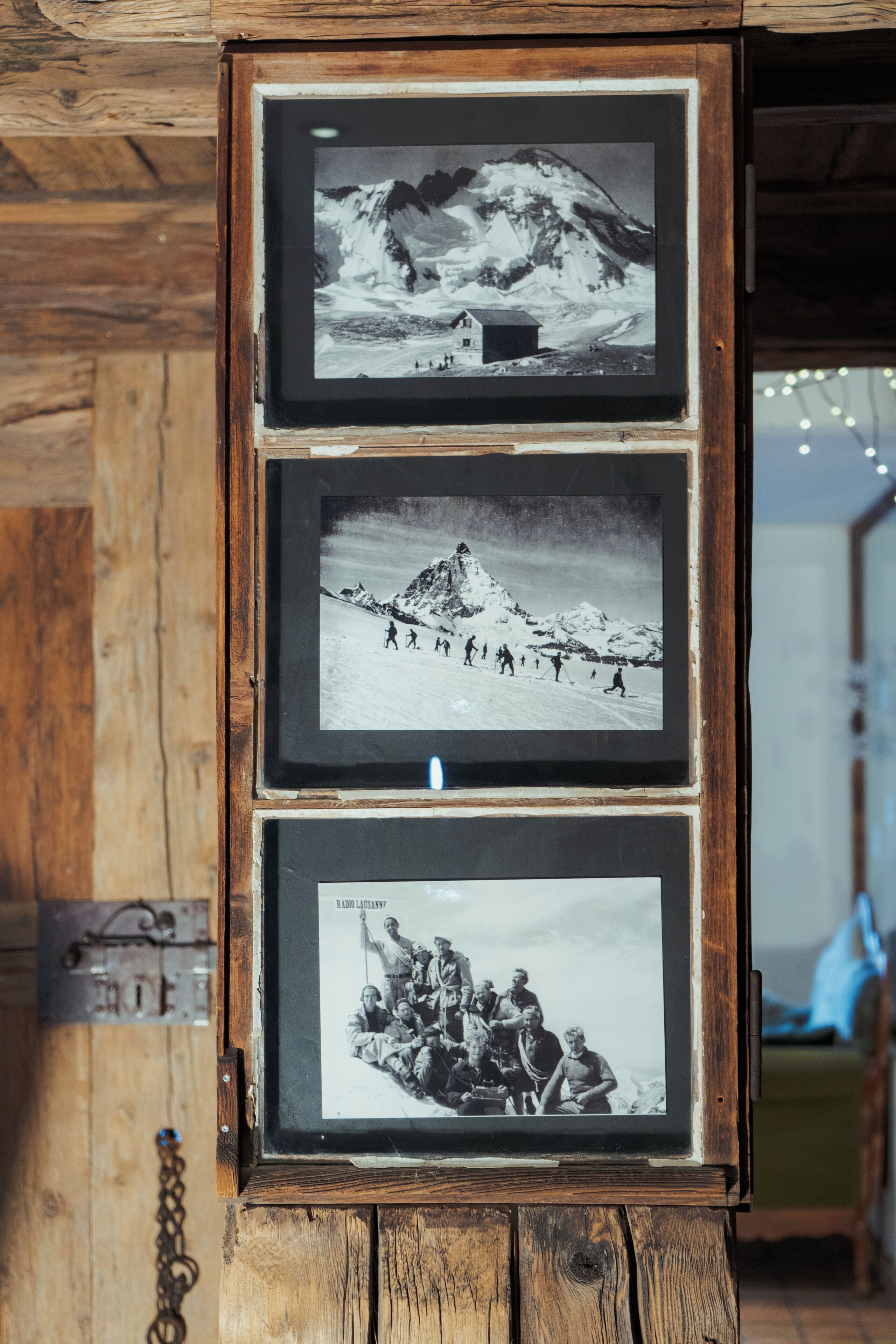 A wooden-framed photo display with three black and white photographs of mountainous landscapes and a group of people.