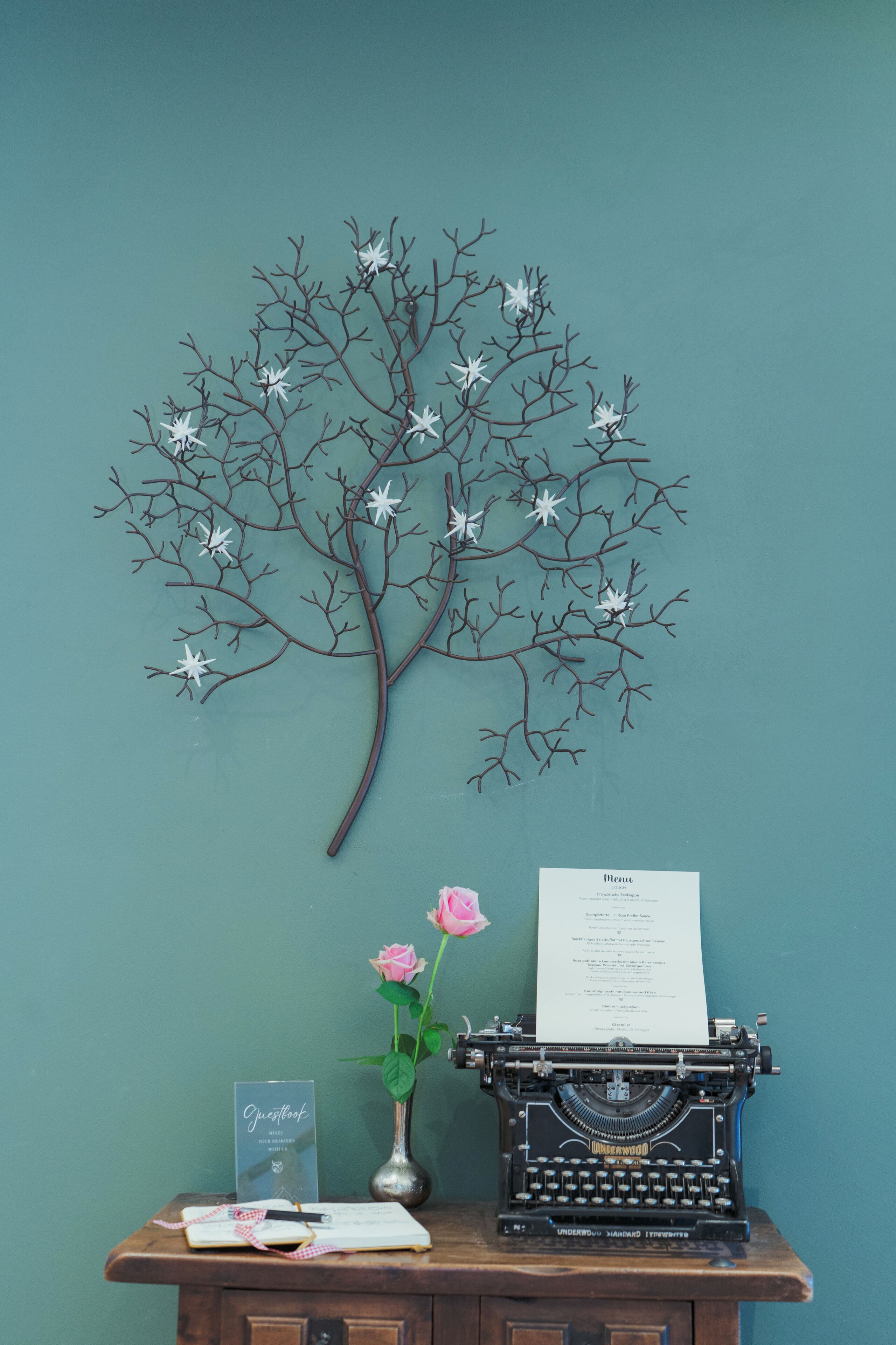 A desk with a typewriter, a vase with flowers, and a menu on the wall.