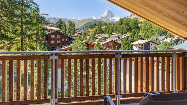 A wooden deck with a view of a mountain town, including houses and a mountain peak.