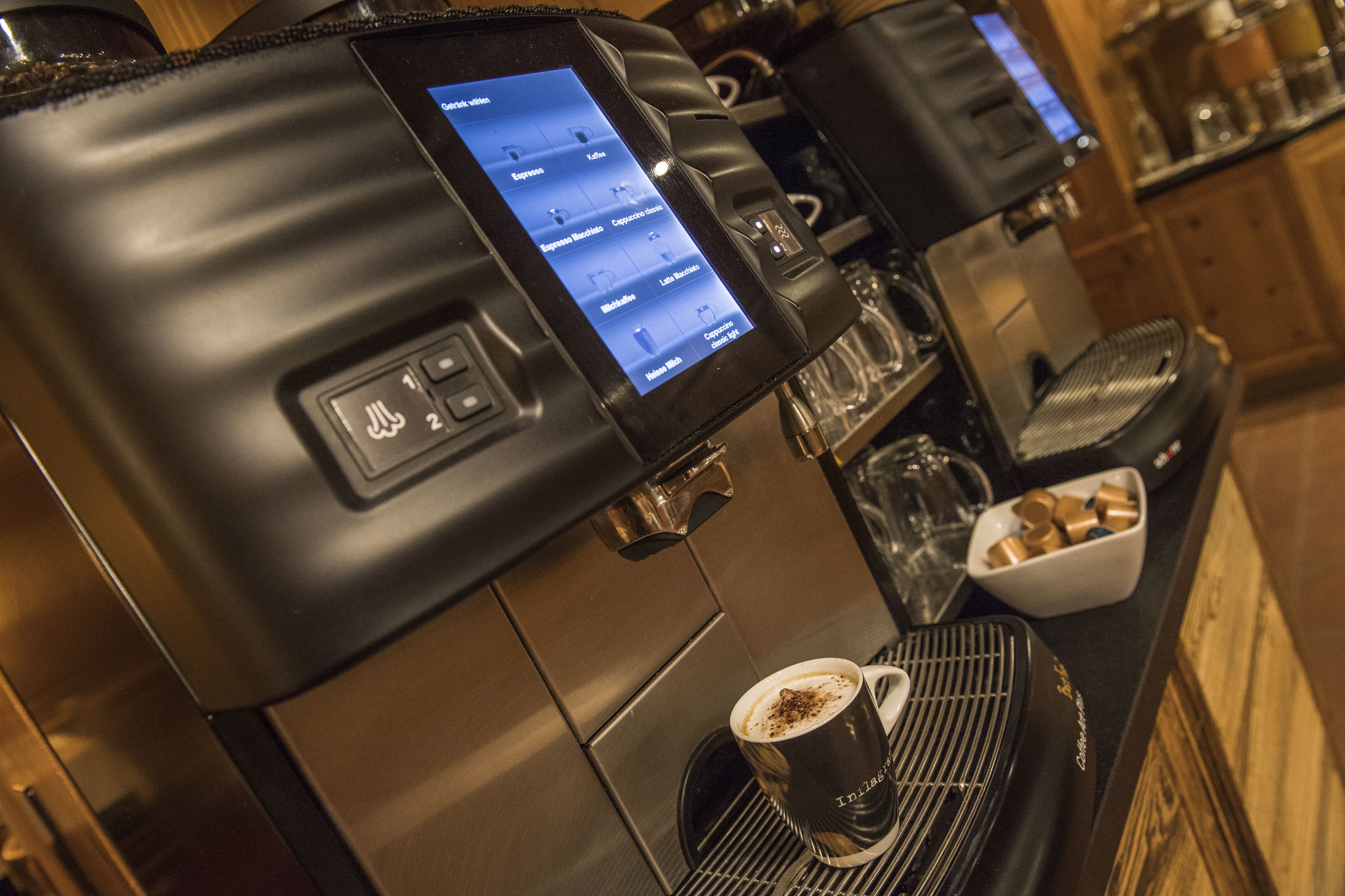A coffee machine with a digital display menu, a cup of coffee, and a coffee grinder.