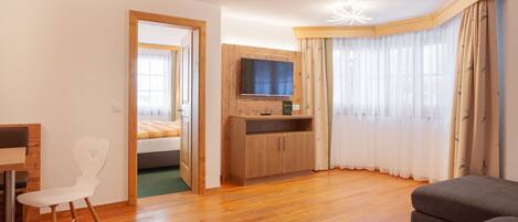 Una habitación moderna con piso de madera, un televisor en un mueble de madera, una silla blanca y una cama con colcha verde.