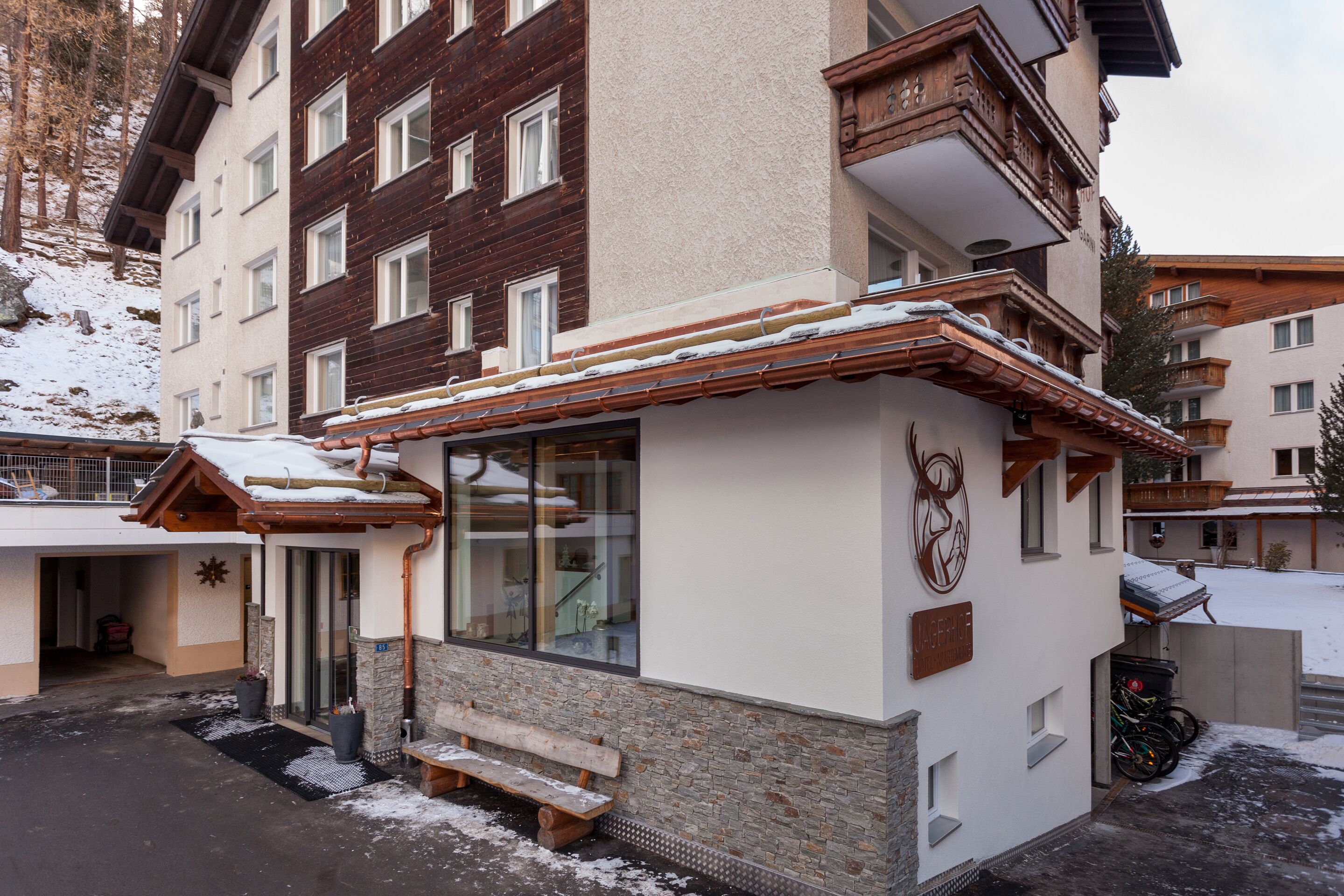 A multi-story building with a snow-covered roof and a wooden bench outside.