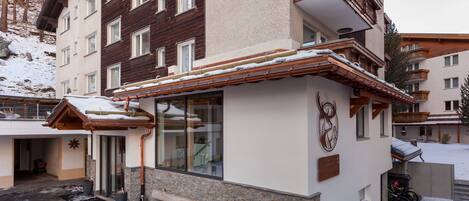 A multi-story building with a snow-covered roof and a wooden bench outside.