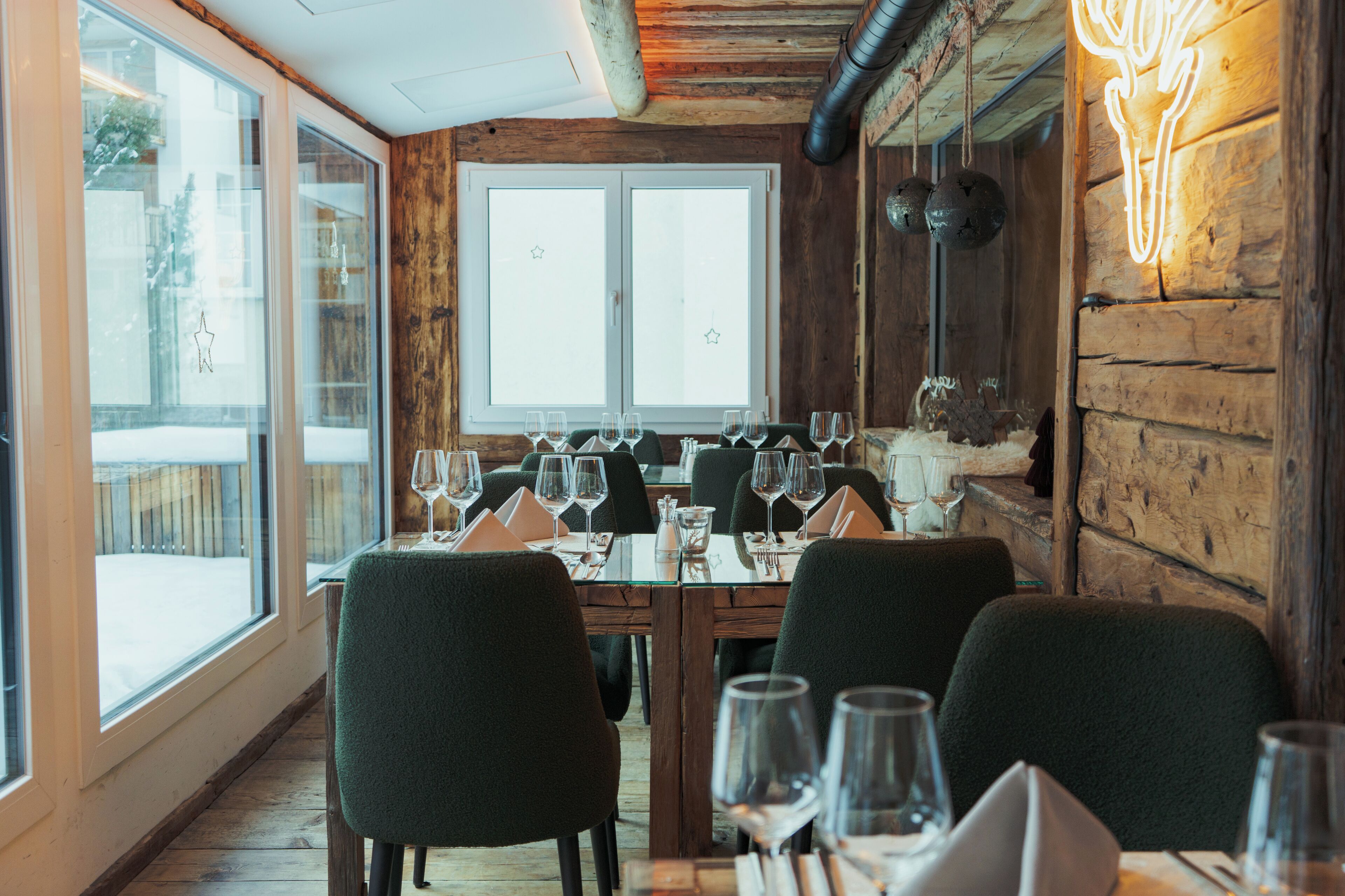 A dining area with wooden walls, large windows, and a table set for multiple guests.