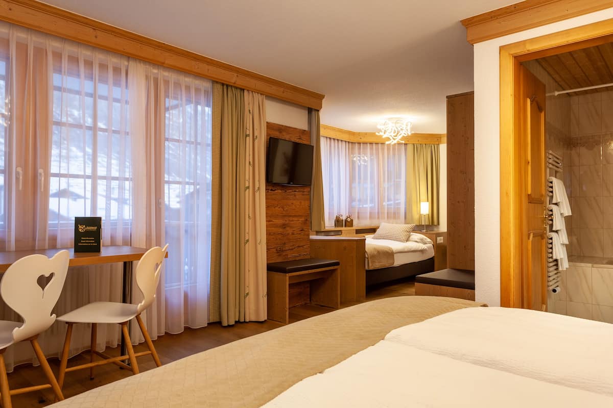 Habitación de hotel con cama, escritorio con silla, televisor montado en la pared y zona de ducha.