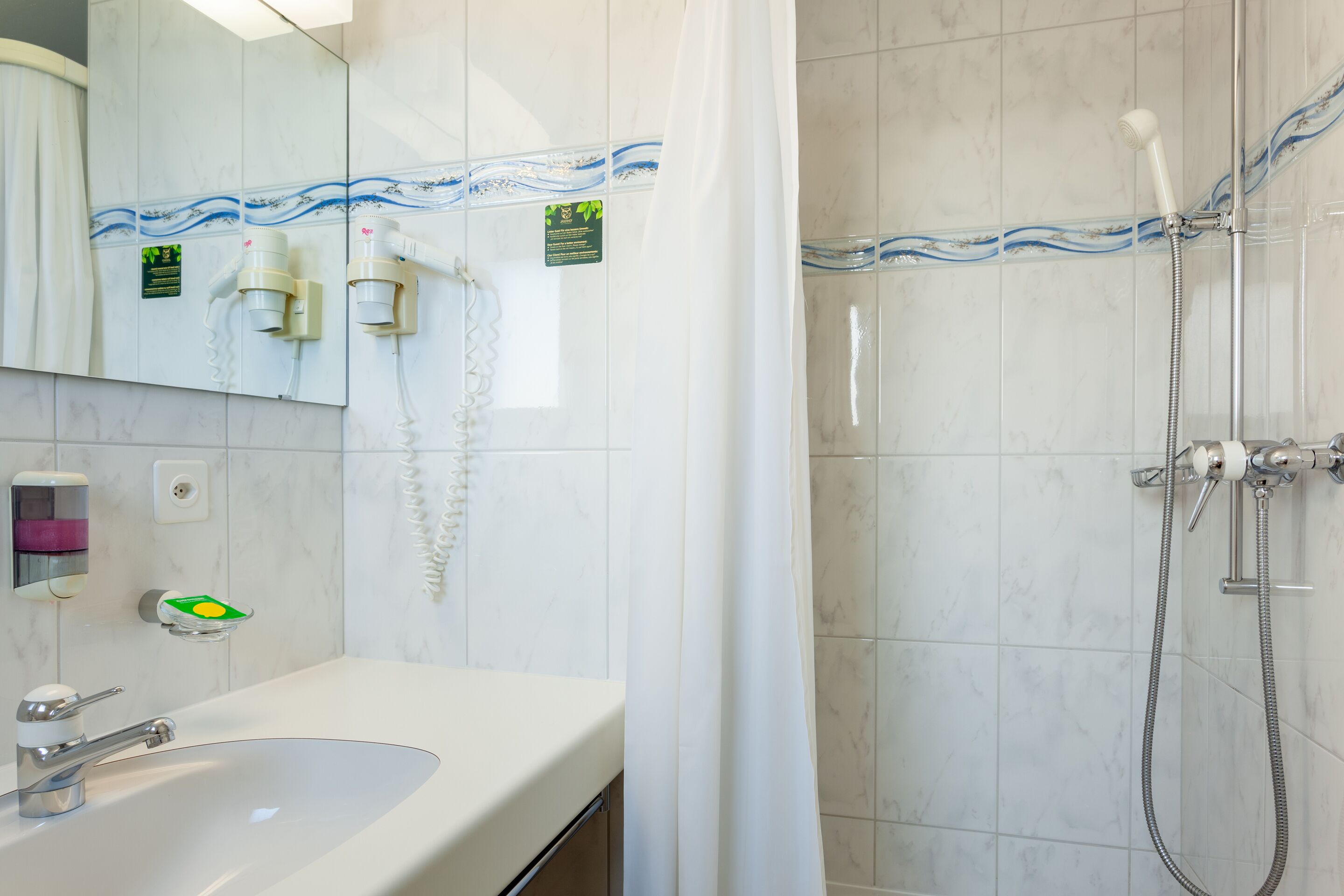 Un bagno con lavandino, specchio, porta asciugamani e doccia con tenda.