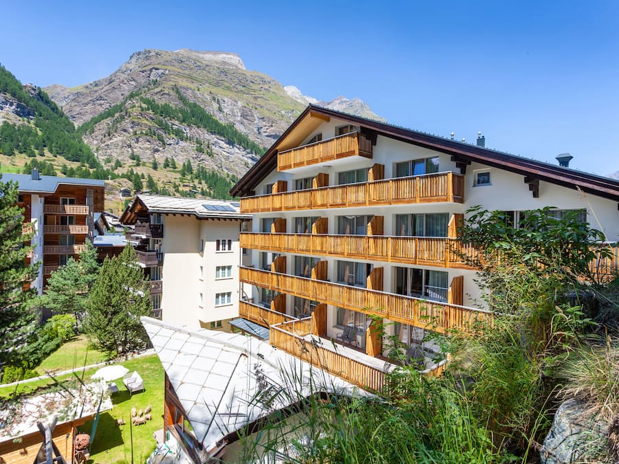 A multi-story hotel with wooden balconies, a garden area, and mountainous views.