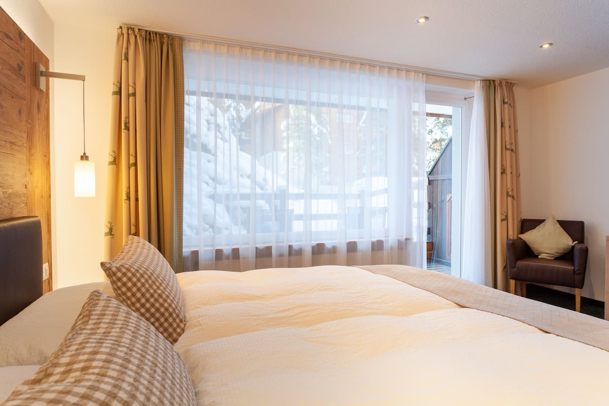 Un dormitorio con una cama grande, una silla y una ventana con cortinas translúcidas.