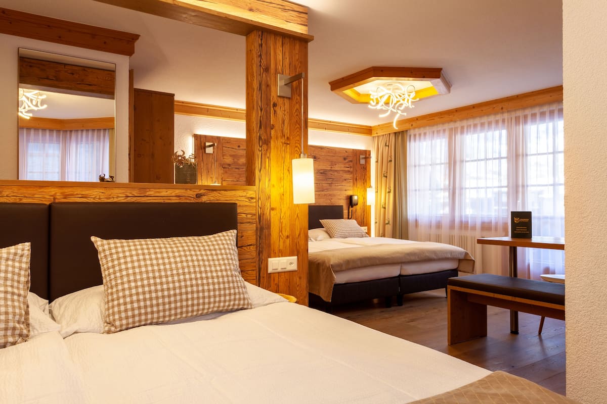 Una habitación de hotel con una cama grande, una cama más pequeña, un banco y un espejo.