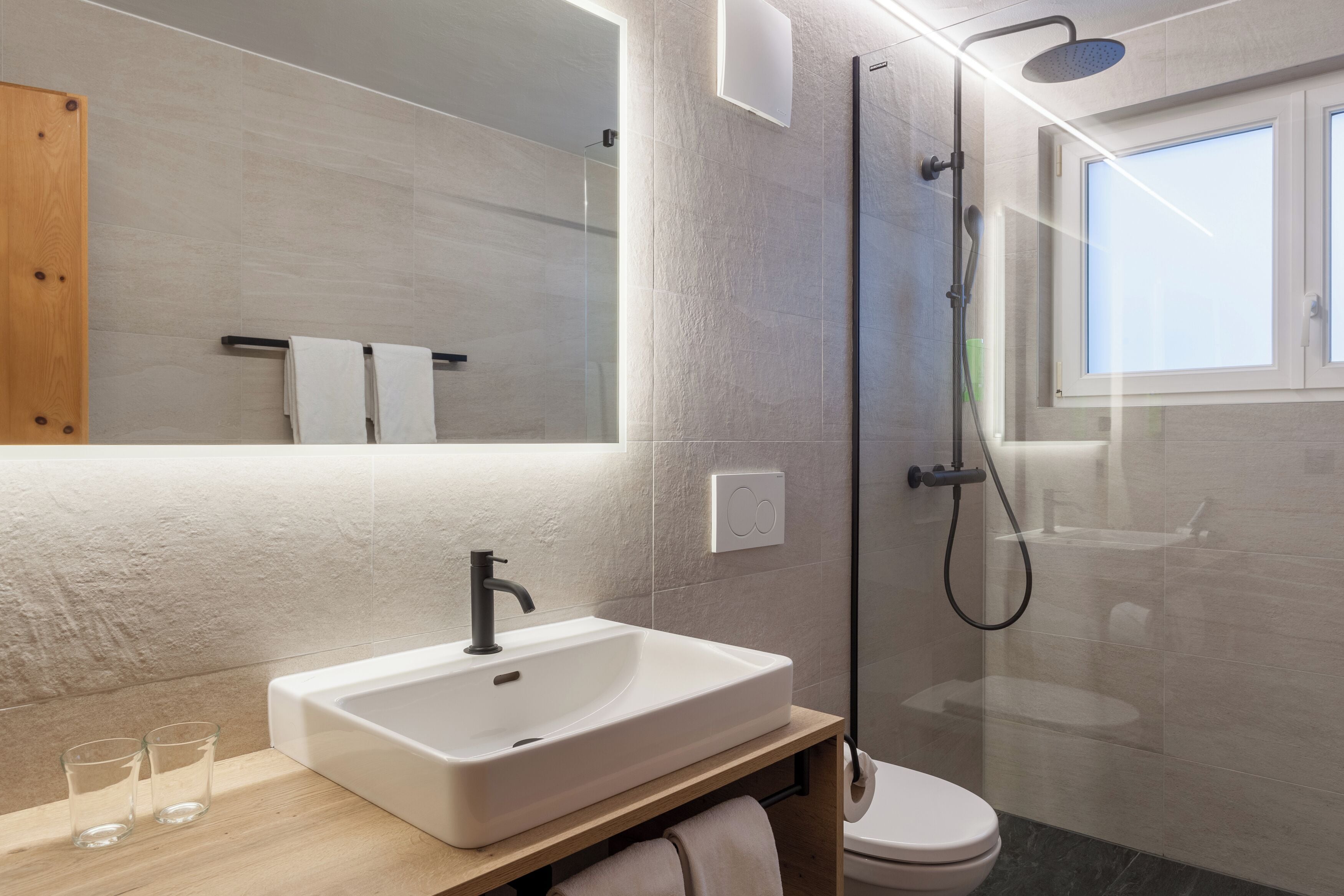 A modern bathroom with a white sink, glass shower enclosure, and a toilet.