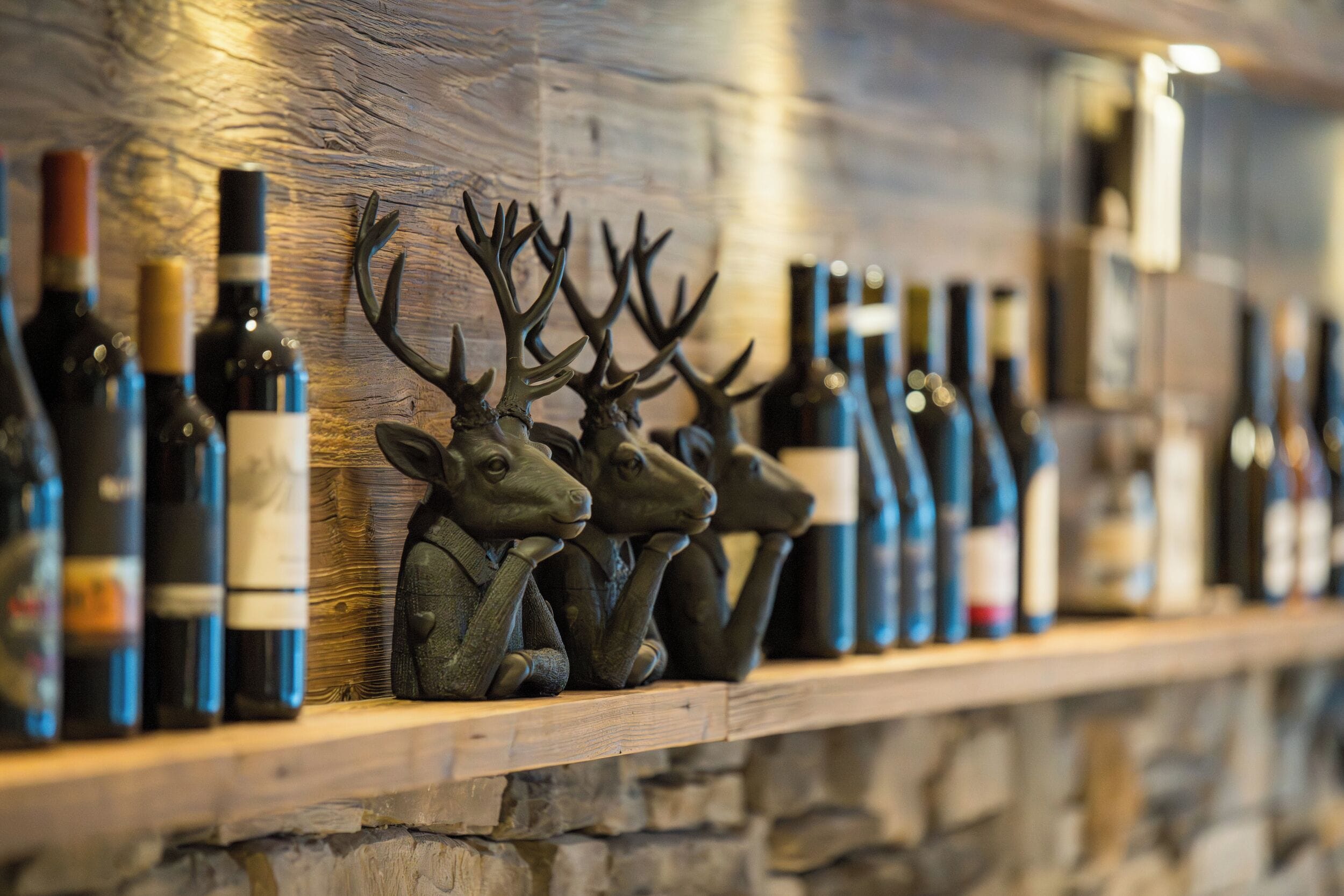 A row of wine bottles on a wooden shelf against a stone wall.